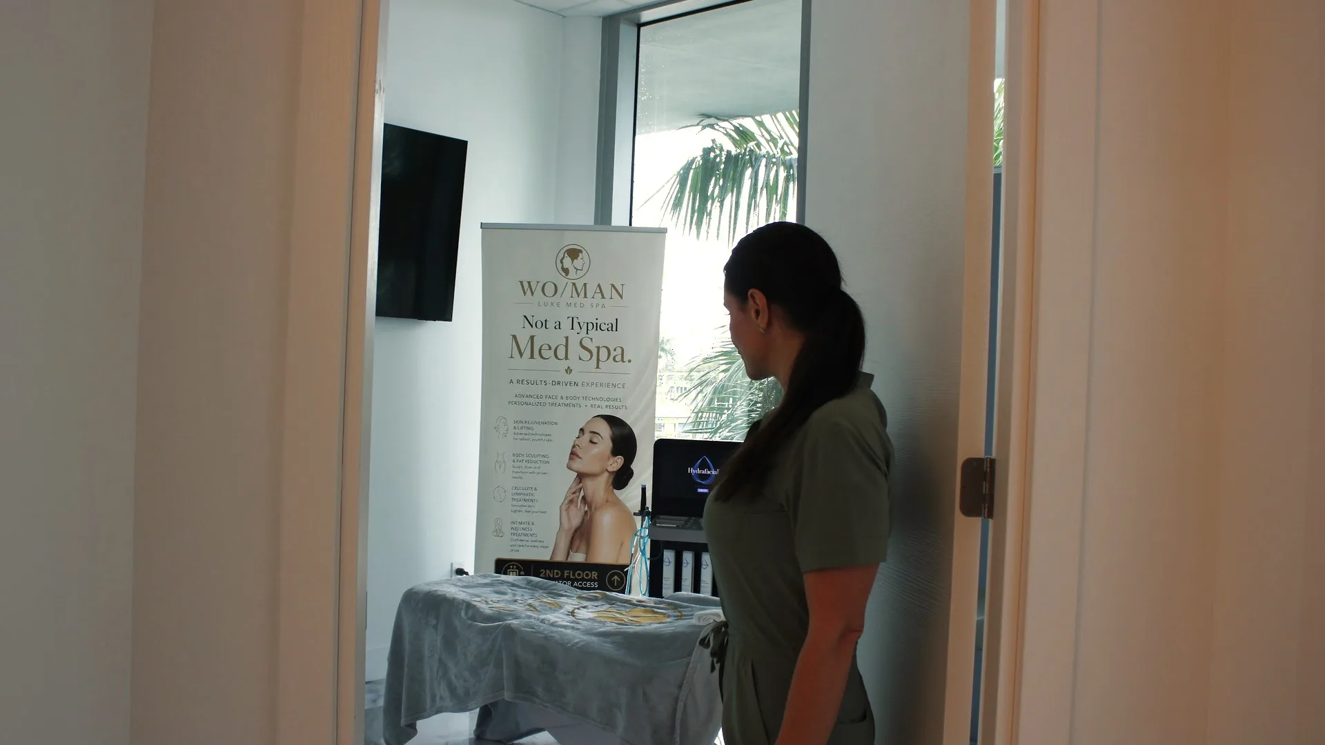 A view through an open door into a private WO/MAN treatment room, a specialist at the door and palms outside the window